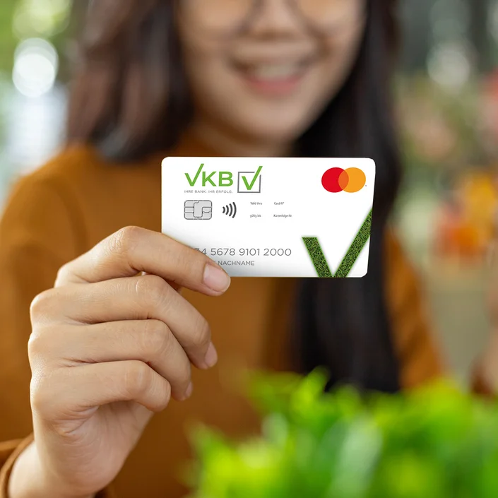 Close-up-Foto: eine junge Frau mit orangfarbenem Shirt hält die weiße VKB-Zukunftskarte in der Hand.