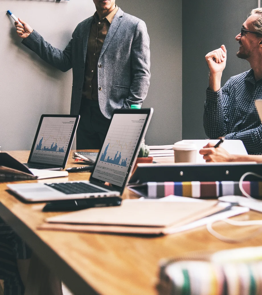 Foto aus einem Besprechungsraum mit mehreren Unterlagen und Laptops am Tisch, die Bildschirme zeigen aktuelle Aktienkurse an.