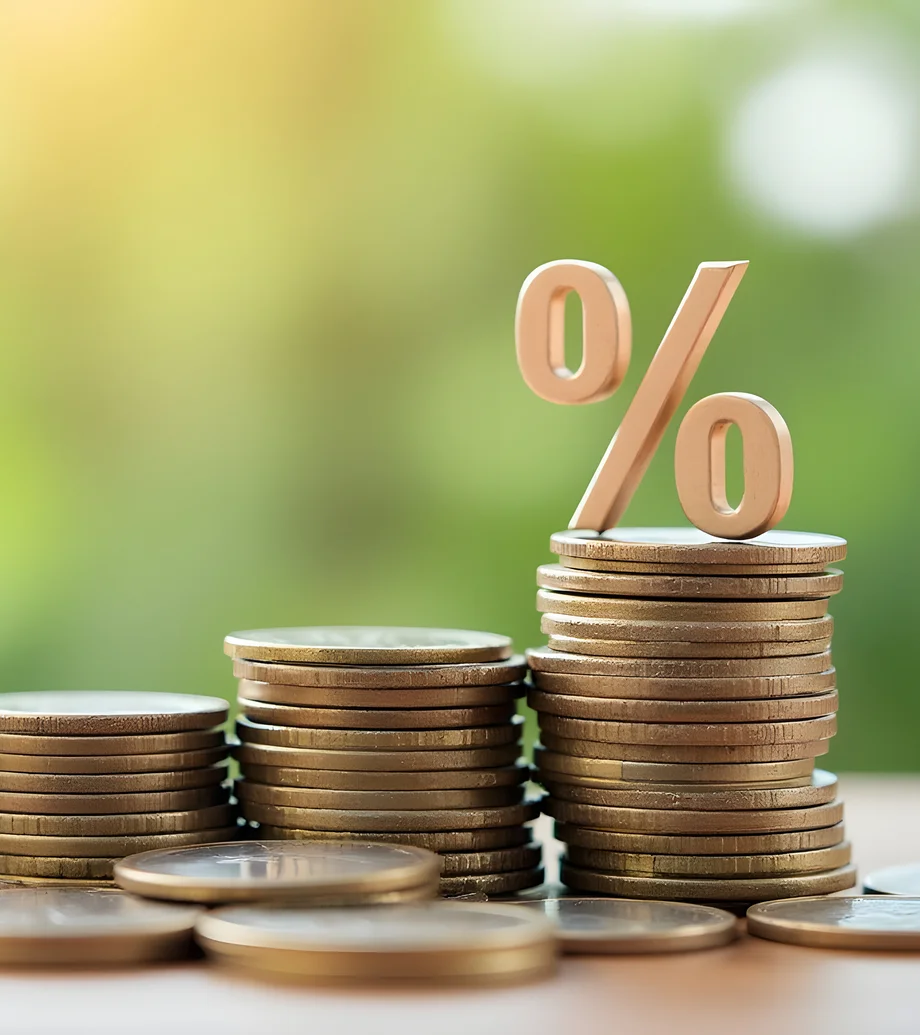 Foto von drei unterschiedlich hohen Münzstapeln, auf dem höchsten ist ein Prozentzeichen platziert, Hintergrund ist grünlich verschwommen.