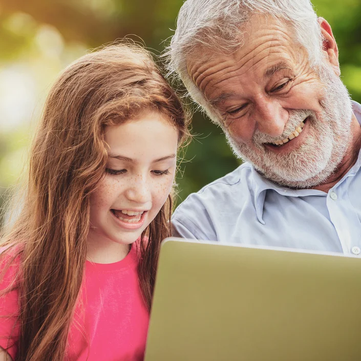 Foto eines älteren Herren mit einem jungen Mädchen, beide schauen auf den Laptop vor sich.