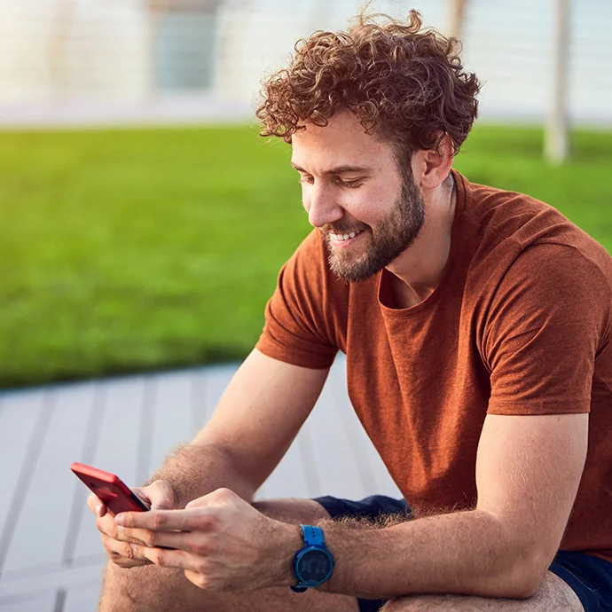 Ein Mann mit lockigem Kurzhaarschnitt und orange-farbenem T-Shirt mit einem Smartphone, sitzend.