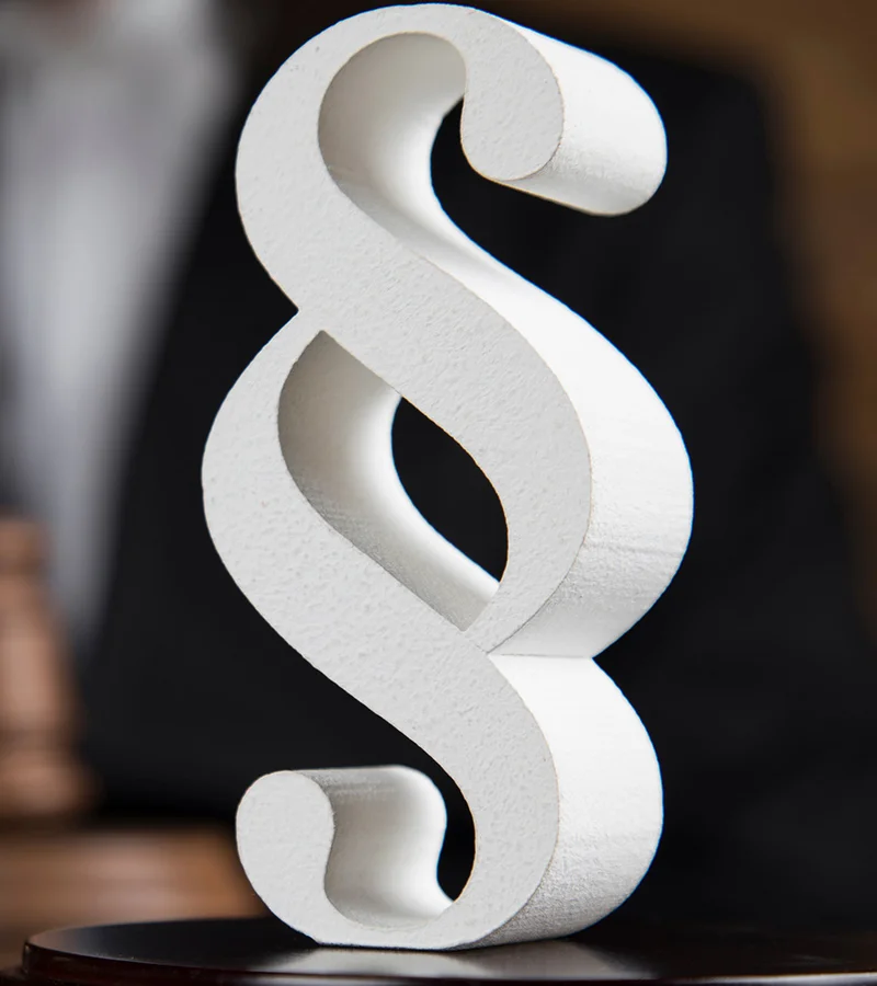 Foto eines weißen Pragraphenzeichen auf dunklem Hintergrund.