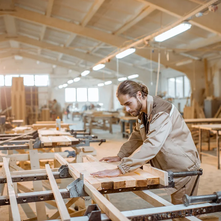 Ein Tischler in einer Halle, der gerade auf einer Werkbank arbeitet.