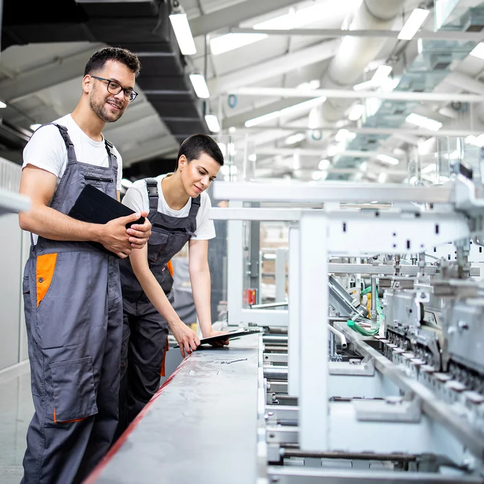 Foto von 2 Arbeitern in einer Halle, die das Ergebnis der Maschine überprüfen.
