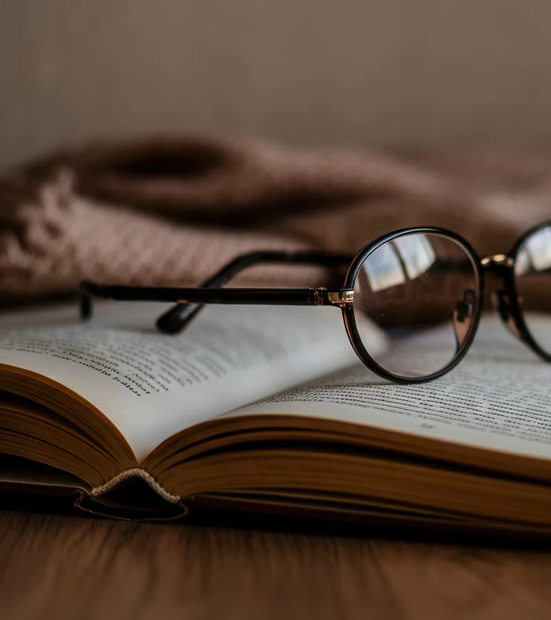 Foto eines aufgeklappten Buches mit einer Lesebrille darauf.