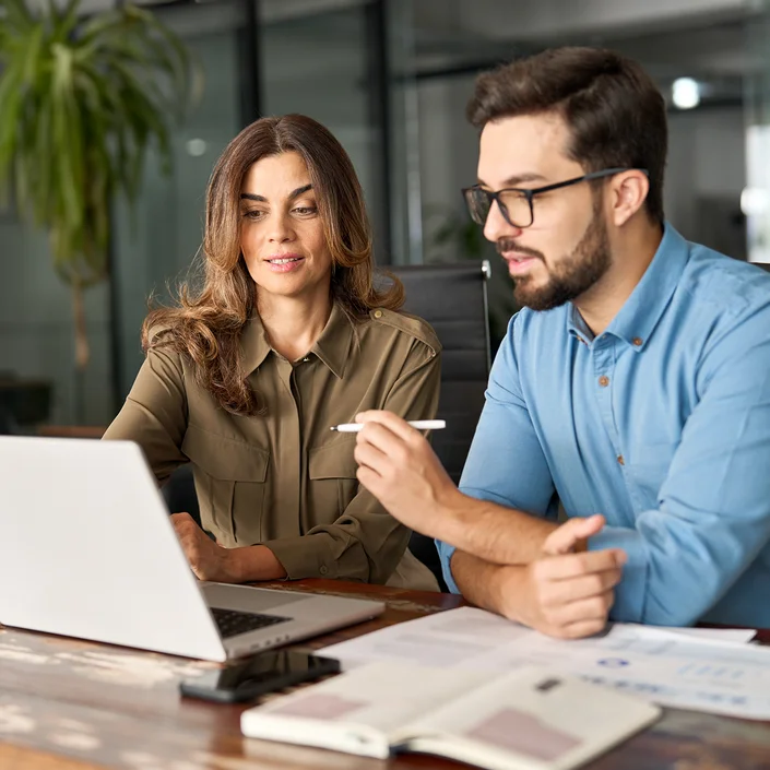Foto von zwei Personen in einem modernen offenen Büro: Ein Mann und eine Frau sitzen vor dem Laptop.