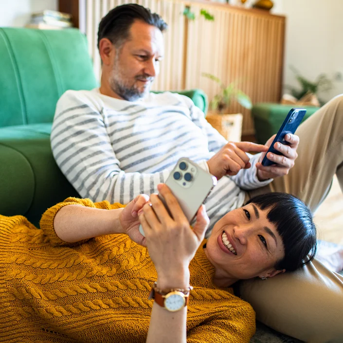 Ein Pärchen zu Hause auf der Couch: Beide halten ein Smartphone in der Hand.