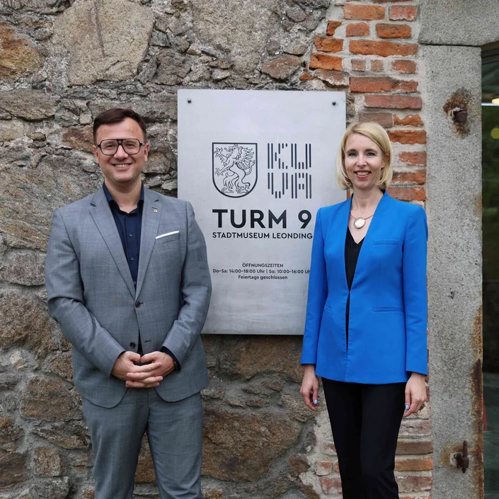 Am Foto: KUVA-Geschäftsführerin Simone Lindinger und VKB-Bereichsdirektor Marketing und Unternehmenskommunikation Almir Barucic vor dem Logo der KUVA im Turm 9 in Leonding.