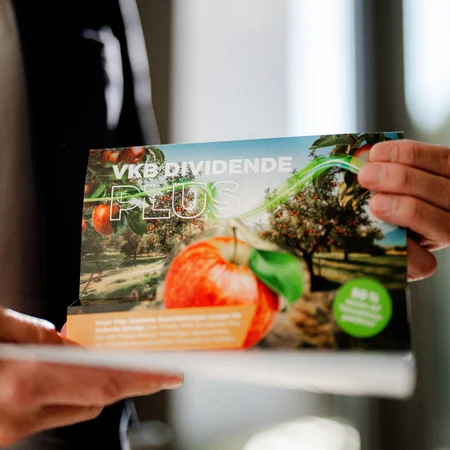 Der Flyer Dividende Plus wird von zwei Händen gehalten
