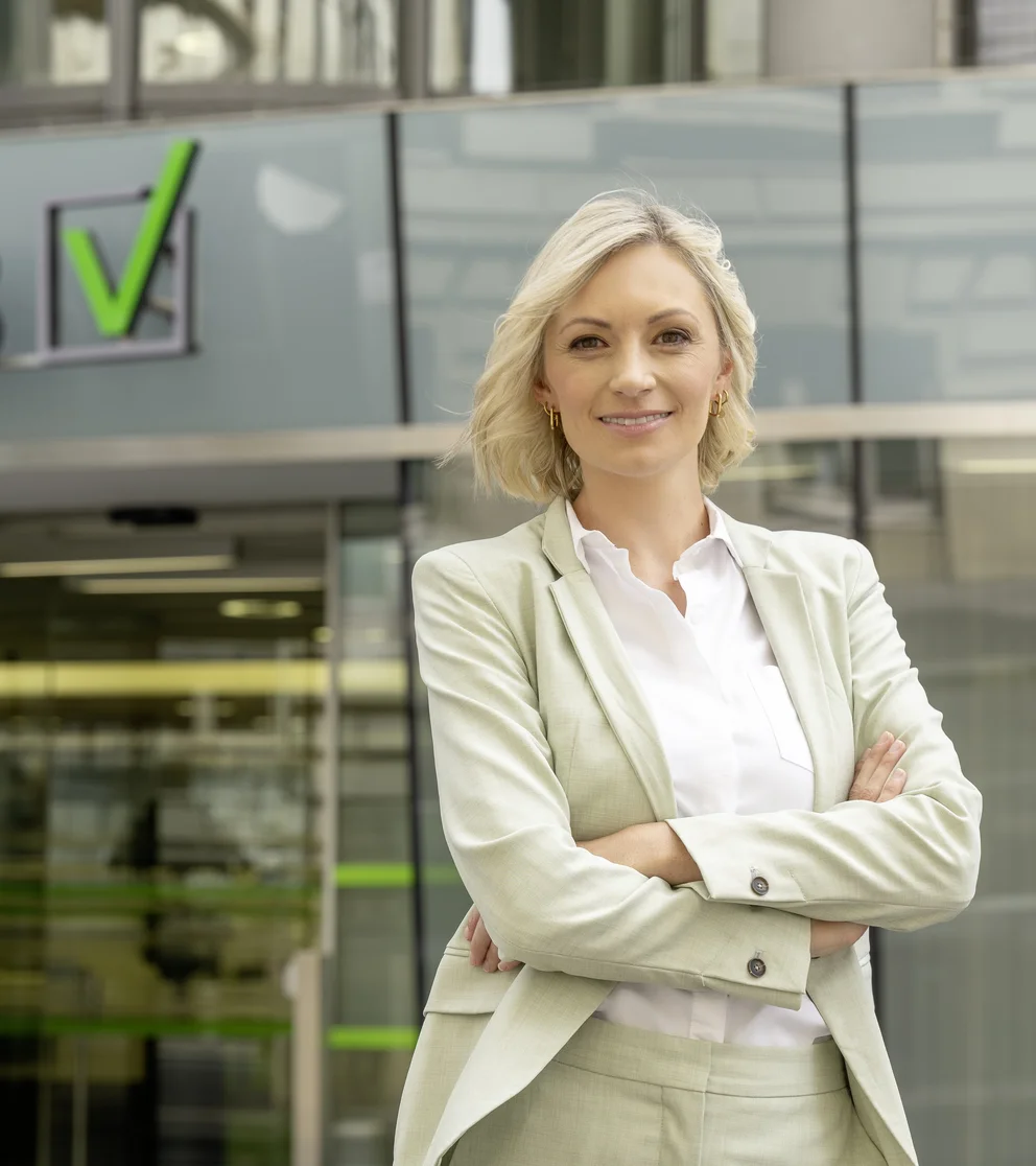 Eine weibliche Person mit blonden Haaren und hellem Hosenanzug vor dem VKB-Kompetenzzentrum in Linz