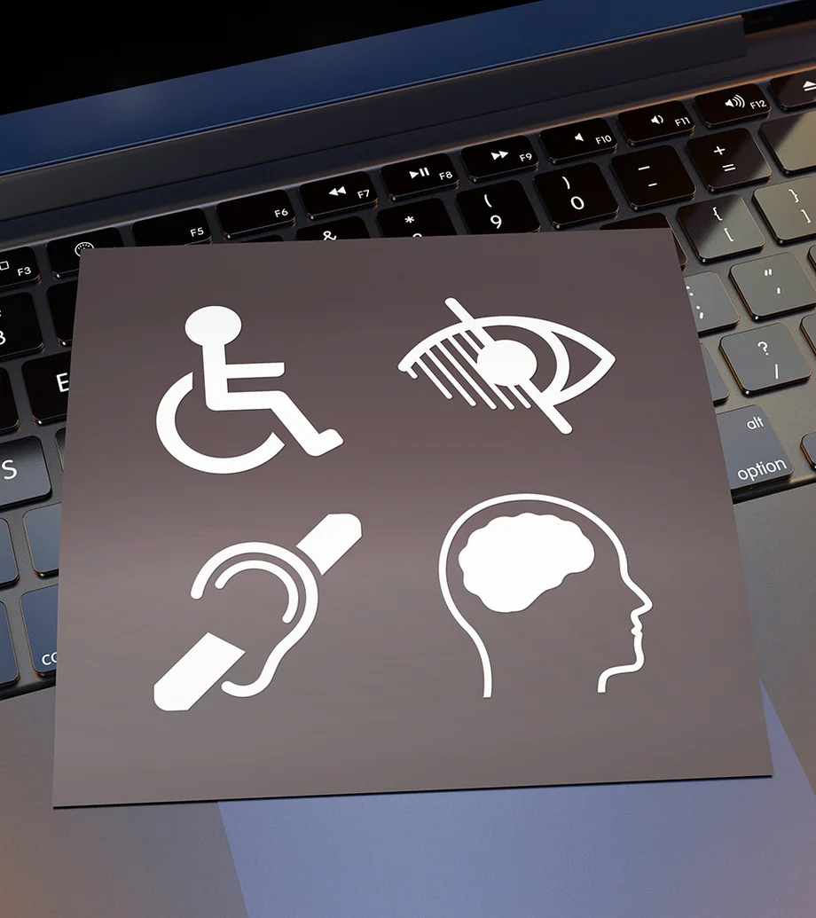 Close-up-Foto eines Laptops, darüber liegt eine Karte mit 4 Symbolen, die Barrierefreiheit darstellen.