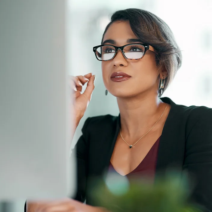 Foto einer Frau im Business-Look mit Brille vor einem PC.