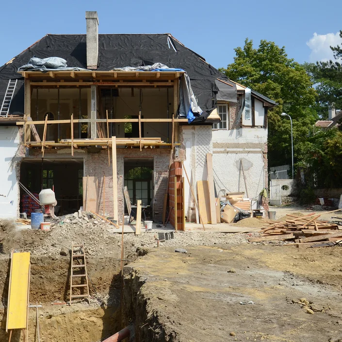 Foto eines alten Hauses, das abgerissen und neu aufgebaut wird. Das Dach ist mit einer Plane abgedeckt und die Fenster und Türen noch nicht wieder eingebaut.