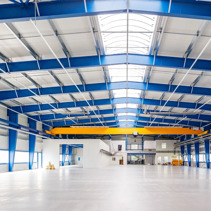 Foto von den Innenräumen einer leeren Lagerhalle mit blauen Stahlträgern.