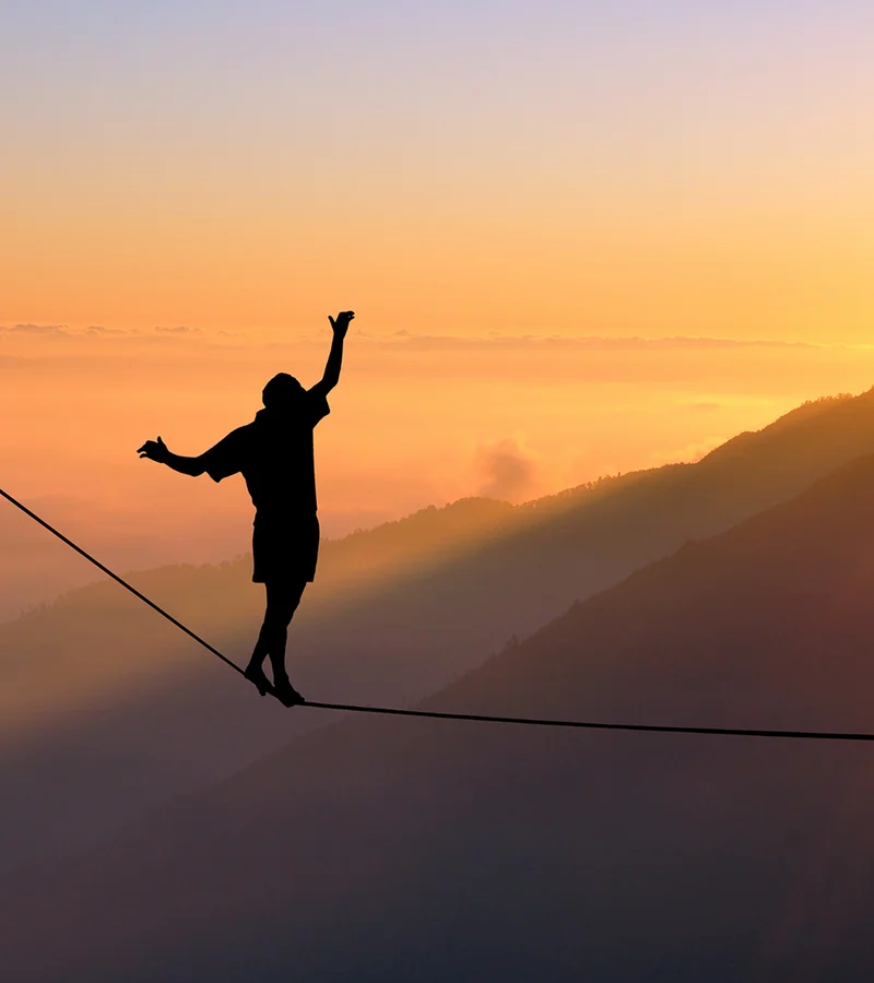 Eine Person bei Sonnenuntergang auf einer Slackline, im Hintergrund ist ein Hügel zu sehen.